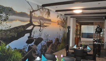 Un restaurante con un mural de un árbol junto a un lago, asientos de piedra y vistas al comedor.