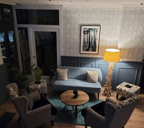 A cozy living room with a blue sofa, patterned armchairs, a wooden coffee table, and a floor lamp. - Parkhotel Schwedt (Schwedt/Oder)