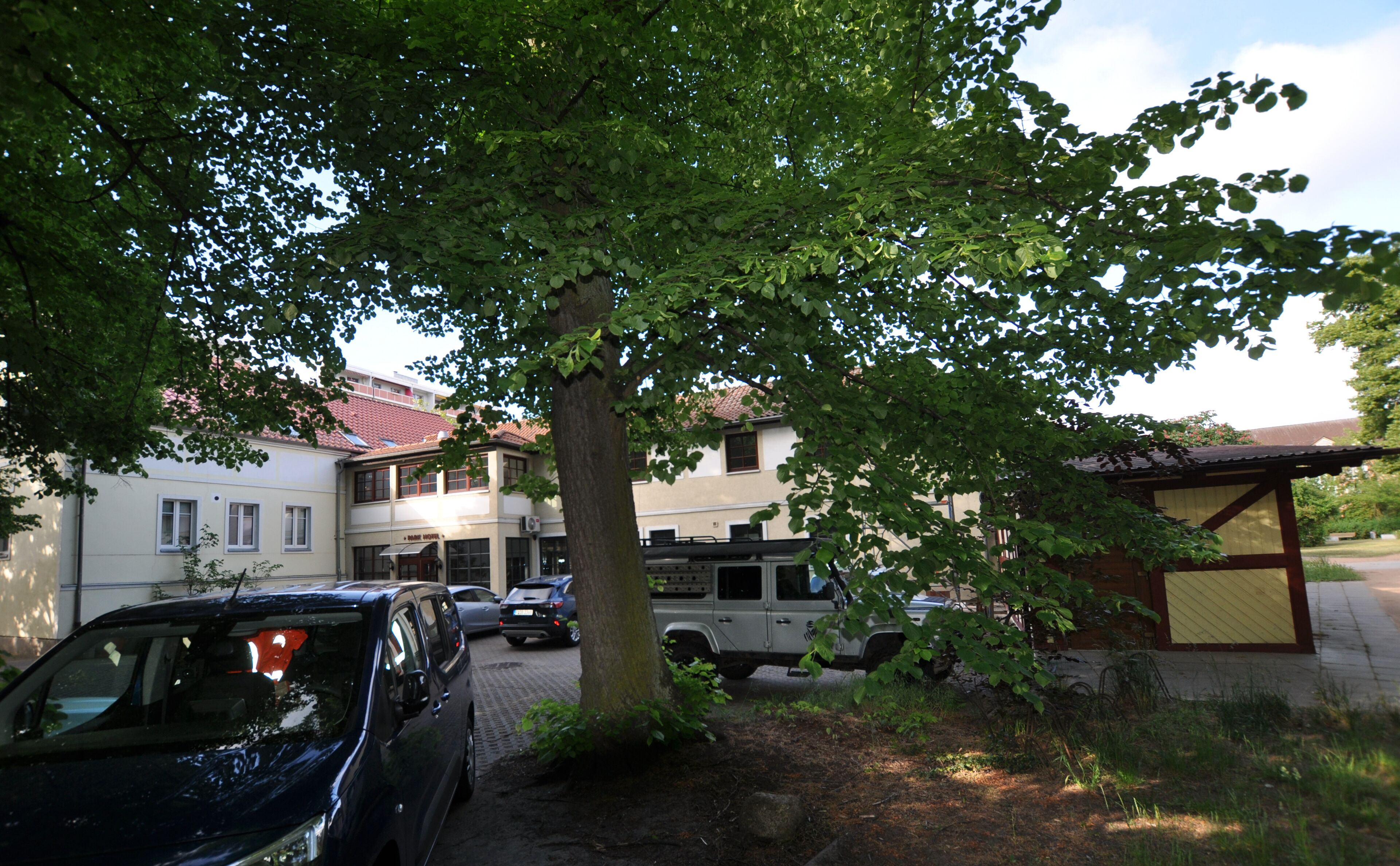 A building with a tiled roof, parked cars, and a tree in front.