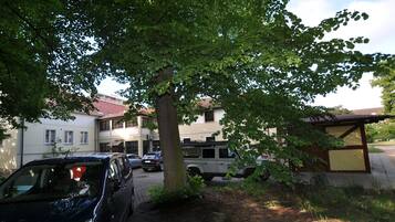 A building with a tiled roof, parked cars, and a tree in front.