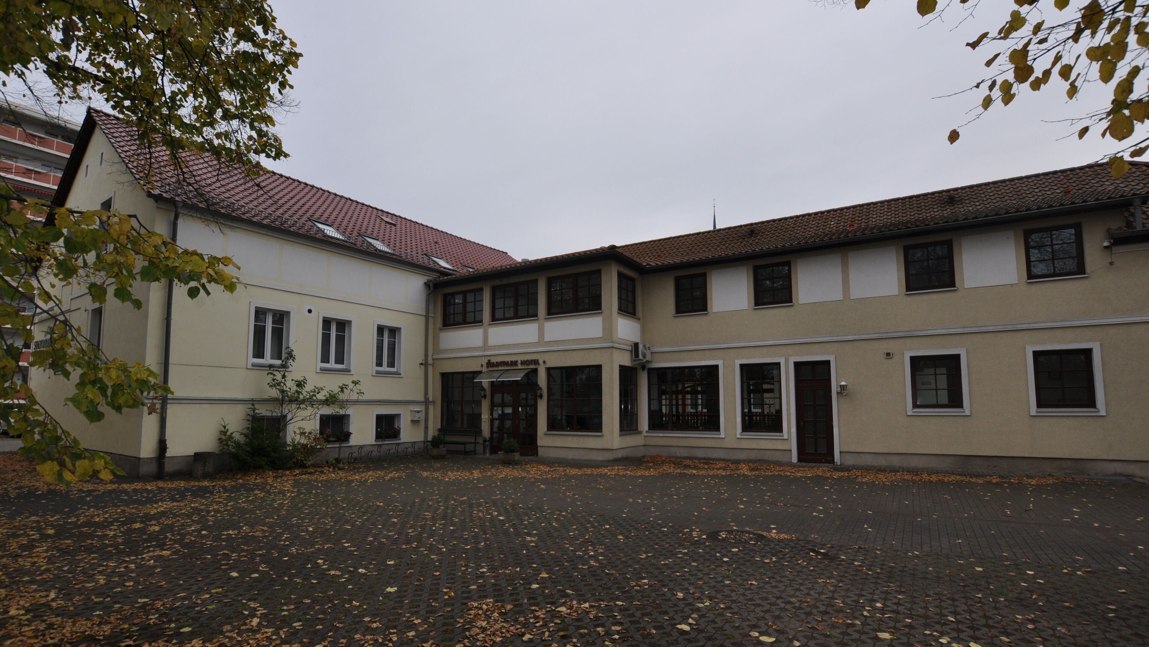 Ein Hotel mit Ziegeldach, einem zentralen Eingang und einem gepflasterten Innenhof mit herabgefallenen Blättern.