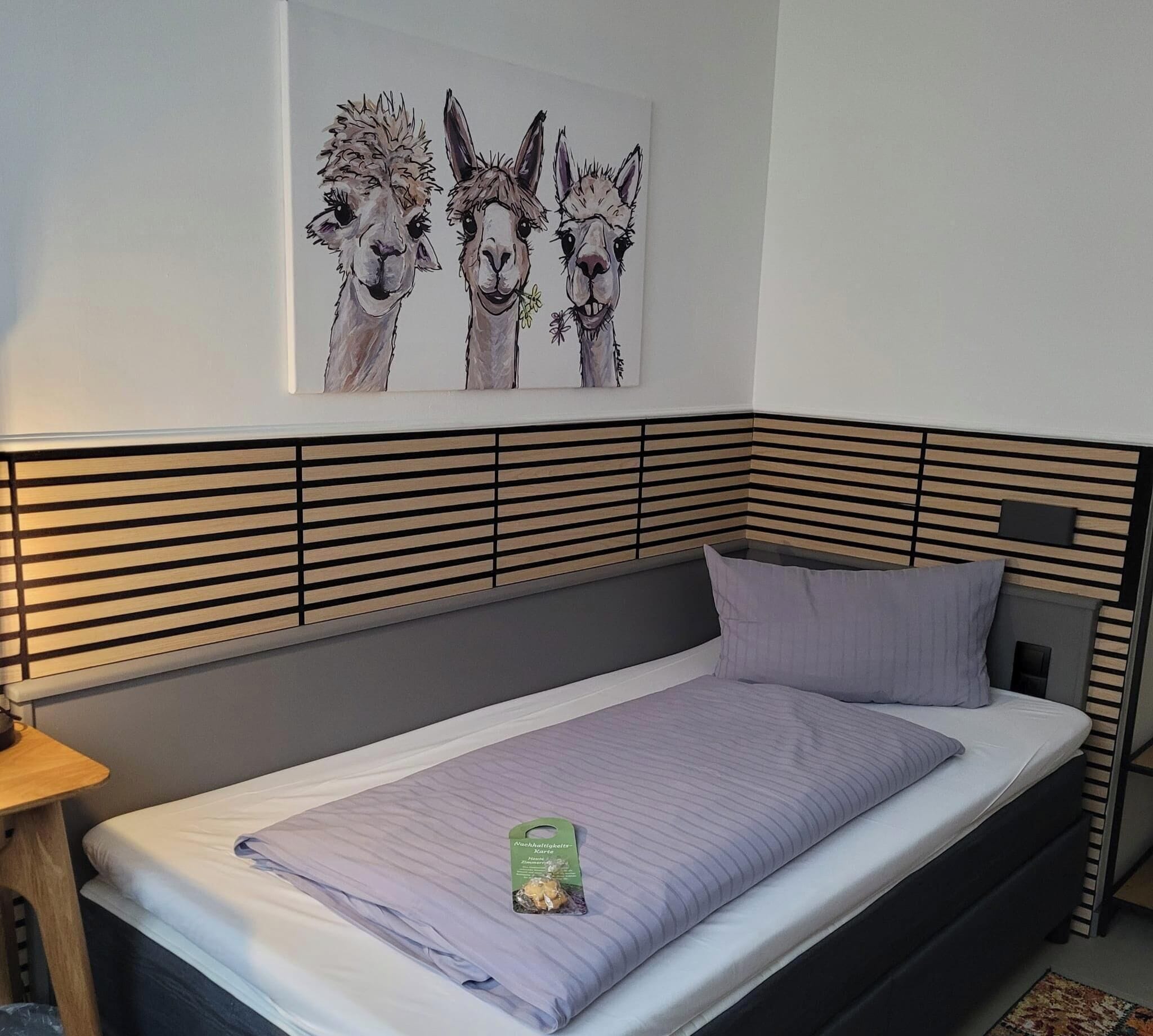 A modern bedroom with a bed, a nightstand, and a wall-mounted artwork of three alpacas.