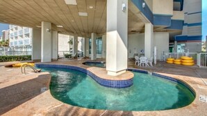 Ein Poolbereich im Freien mit bogenförmigem Design, umgeben von einer Betonplattform und einem überdachten Bereich mit Sitzgelegenheiten.