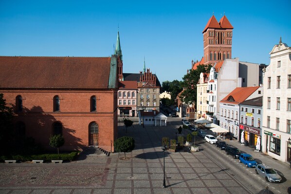 A square with cobblestone pavement, historic buildings, and a prominent church with a tall spire. - Apartament Astro (Torun)