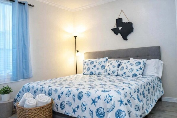 Ein Schlafzimmer mit einem Bett, einer Wanddekoration mit der texanischen Flagge, einer Nachttischlampe und einem Korb mit Handtüchern.