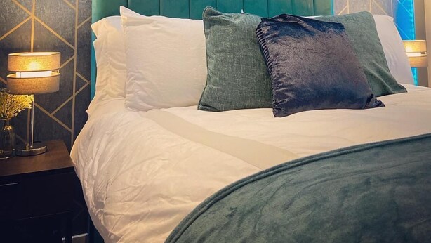 Un lit avec une tête de lit recouverte d’un tissu turquoise, une literie blanche et plusieurs oreillers.