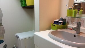 A bathroom with a white sink, a mirror, and a toilet. There are toiletries on a shelf and a trash bin. - SHARED ROOM (Rennes)
