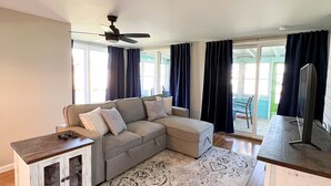 A living room with a sectional sofa, a small cabinet, a patterned rug, and a ceiling fan. - Newly Remodeled Cabin Steps from Sylvan Lake (Rome City)