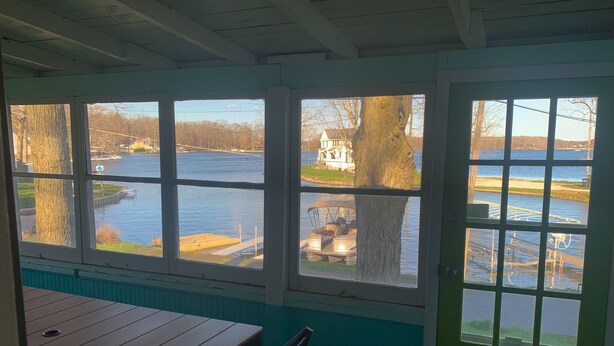 A room with a table and chairs, large windows with a view of a lake, a green door, and a white ceiling. - Newly Remodeled Cabin Steps from Sylvan Lake (Rome City)