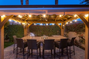 Relax in a serene outdoor space with a pergola, string lights, and a round table for dining or socializing.