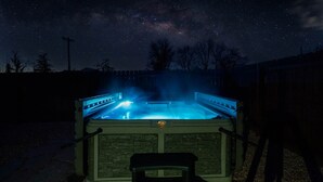 Ein Whirlpool mit Blick auf den Nachthimmel, umgeben von Bäumen und einem Zaun.