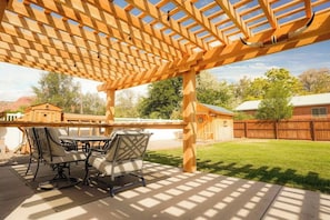 A covered patio with a wooden pergola, outdoor furniture, and a view of a backyard with a wooden fence and a house. - Kanab Retreat | Hot Tub, Fire Pit & Zion Access (Kanab)