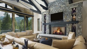 Un salon moderne avec une cheminée en pierre, des canapés en cuir et une grande fenêtre donnant sur un paysage montagneux.