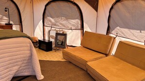 A tented room with a bed, a sofa, a small table, and a framed picture.