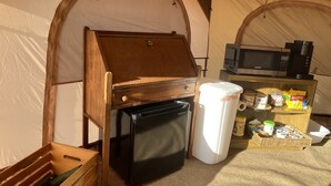 A compact kitchen area with a refrigerator, microwave, and storage cabinet inside a tent.
