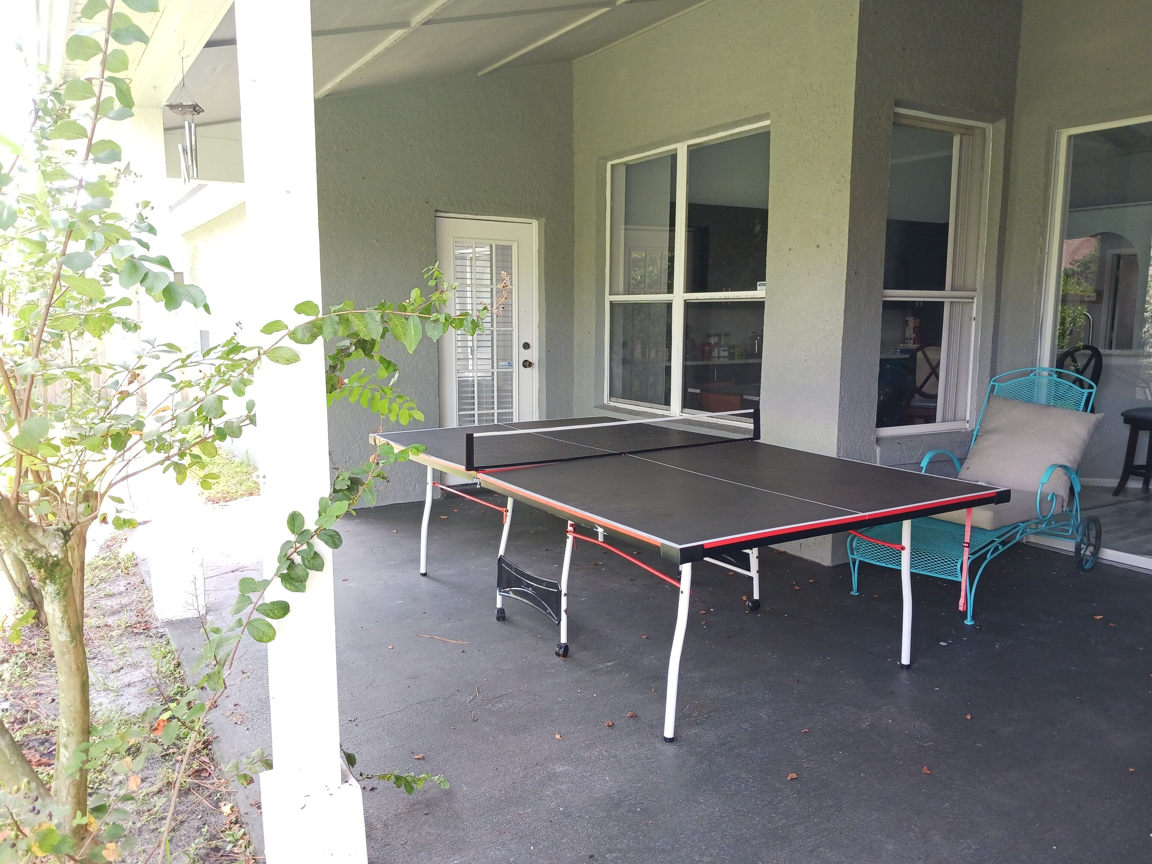 Een tafeltennistafel buiten met een stoel, een deur en ramen op de achtergrond.