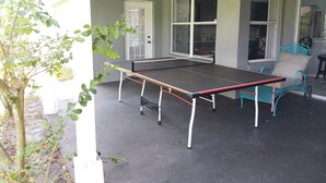 An outdoor table tennis table with a chair, a door, and windows in the background. - LOVE NEST--NEWLY RENOVATED Sleeps 7--CLOSE TO DOWNTOWN, AIRPORT & ATTRACTIONS (Orlando)