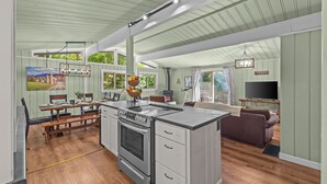 A spacious kitchen with a central island, wooden dining table, and a cozy living area with a sofa and TV.
