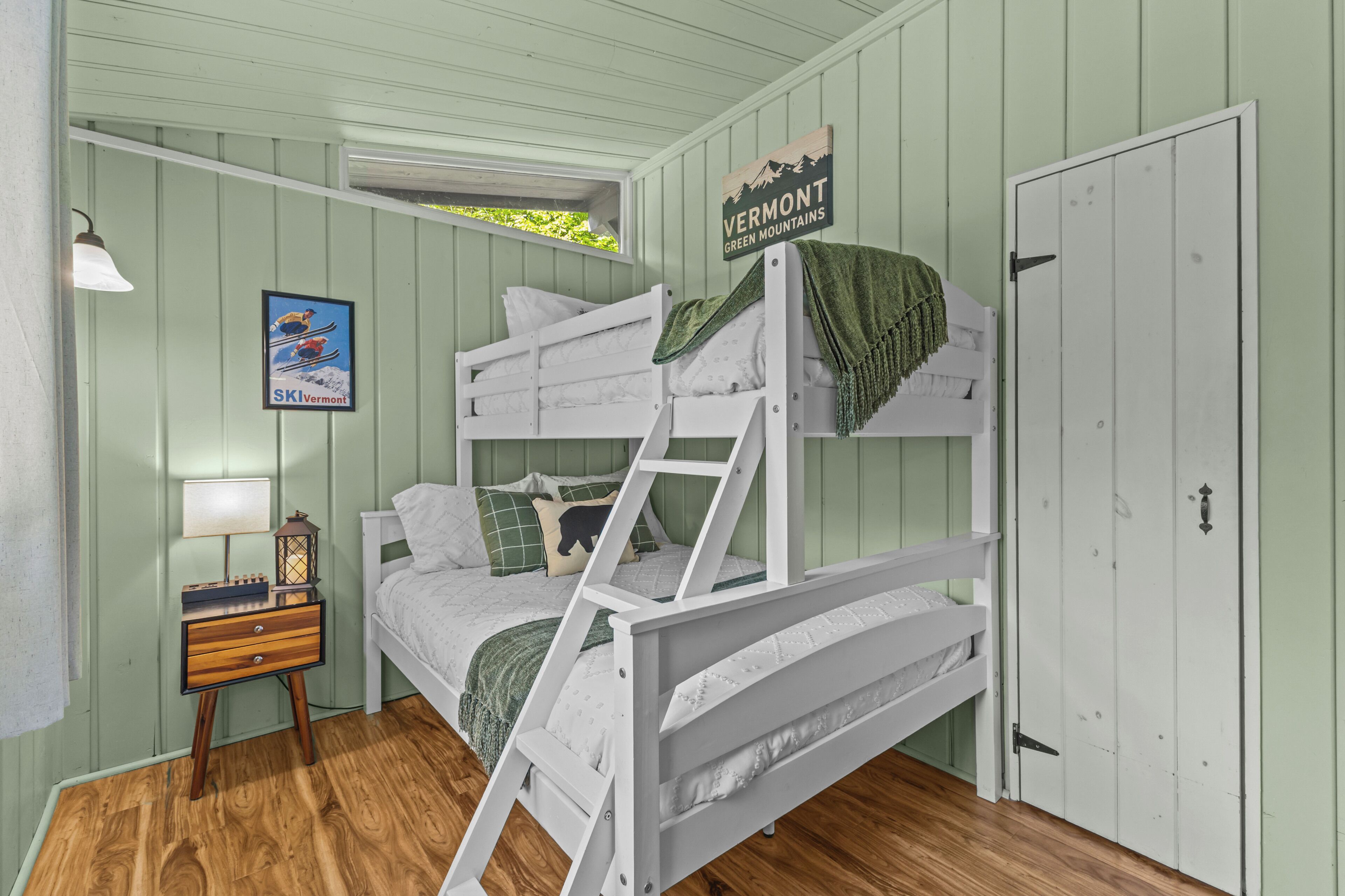 A bunk bed with a ladder, a nightstand with a lamp, a framed picture, and a door with a sign.
