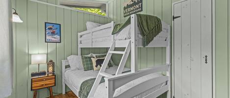 A bunk bed with a ladder, a nightstand with a lamp, a framed picture, and a door with a sign.