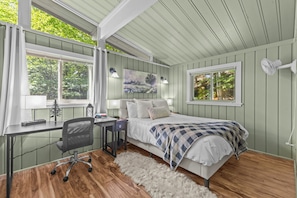Un dormitorio con cama, escritorio, silla y un ventanal con cortinas.