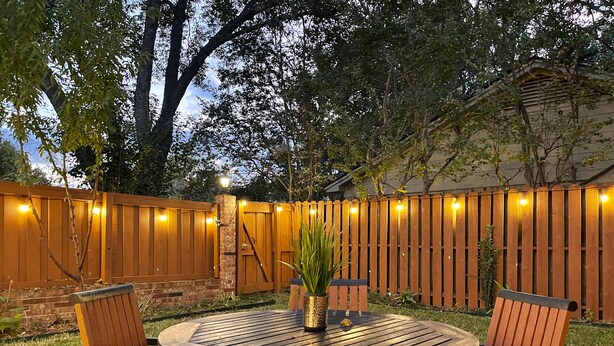 An outdoor patio with a round table and four wooden chairs, surrounded by a wooden fence and a brick wall. - Pets Welcome! HOT TUB, Games, Backyard, Free Wine, WiFi, 4 TVs (Richardson)