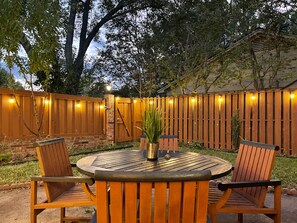Une terrasse extérieure avec une table ronde et quatre chaises en bois, entourée d’une clôture en bois et d’un mur en briques.