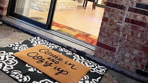 A modern entrance with a glass door, a brick wall, and a welcome mat. - Pets Welcome! HOT TUB, Games, Backyard, Free Wine, WiFi, 4 TVs (Richardson)