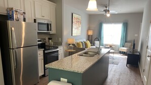 A modern kitchen with stainless steel appliances, a granite countertop island, and a view to the living area. - Valdosta Oasis: 2BR 2.5 BA near VSU and Downtown (Valdosta)