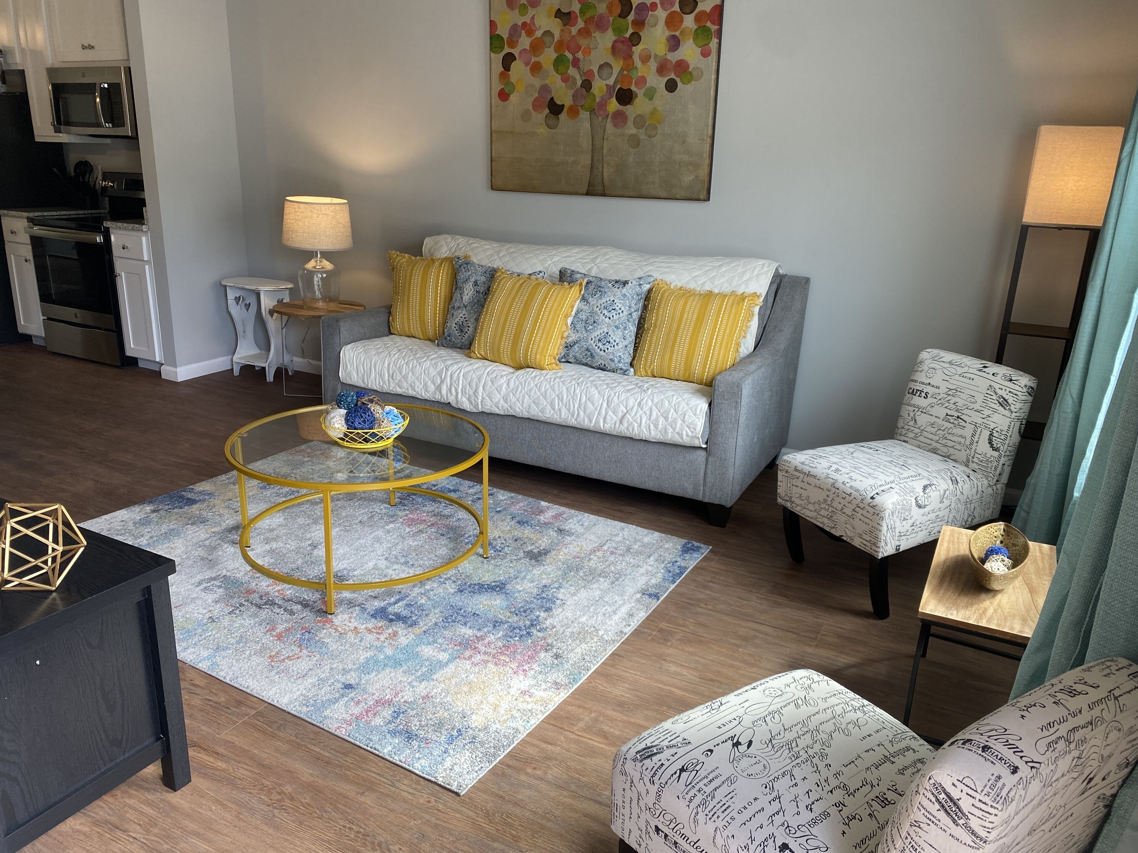 A modern living room with a grey sofa, yellow and blue patterned cushions, a round coffee table, and a patterned armchair.