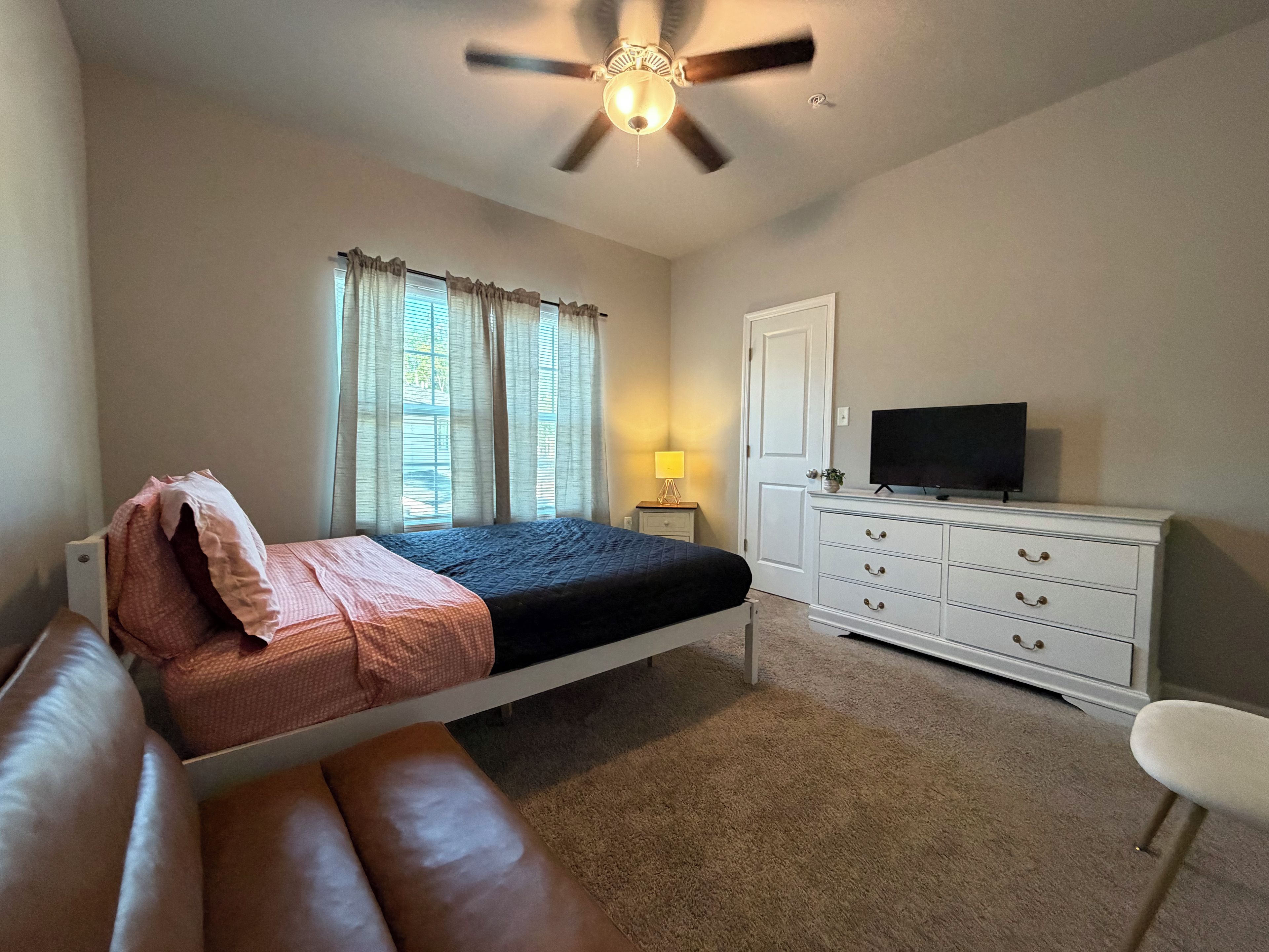 A bedroom with a bed, a dresser, a television, and a ceiling fan.