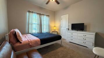 A bedroom with a bed, a dresser, a television, and a ceiling fan.