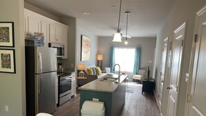 A modern kitchen with a central island, a refrigerator, and a stove. There is a dining area with yellow placemats and a table. - Valdosta Oasis: 2BR 2.5 BA near VSU and Downtown (Valdosta)
