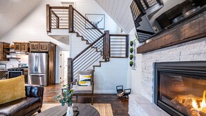 A modern living room with a fireplace, a dining area, and a kitchen with wooden cabinets and a stainless steel refrigerator.