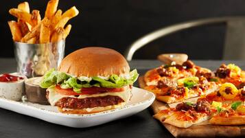 Een hamburger met sla, tomaat en kaas, een bord met friet en een pizza met diverse toppings.