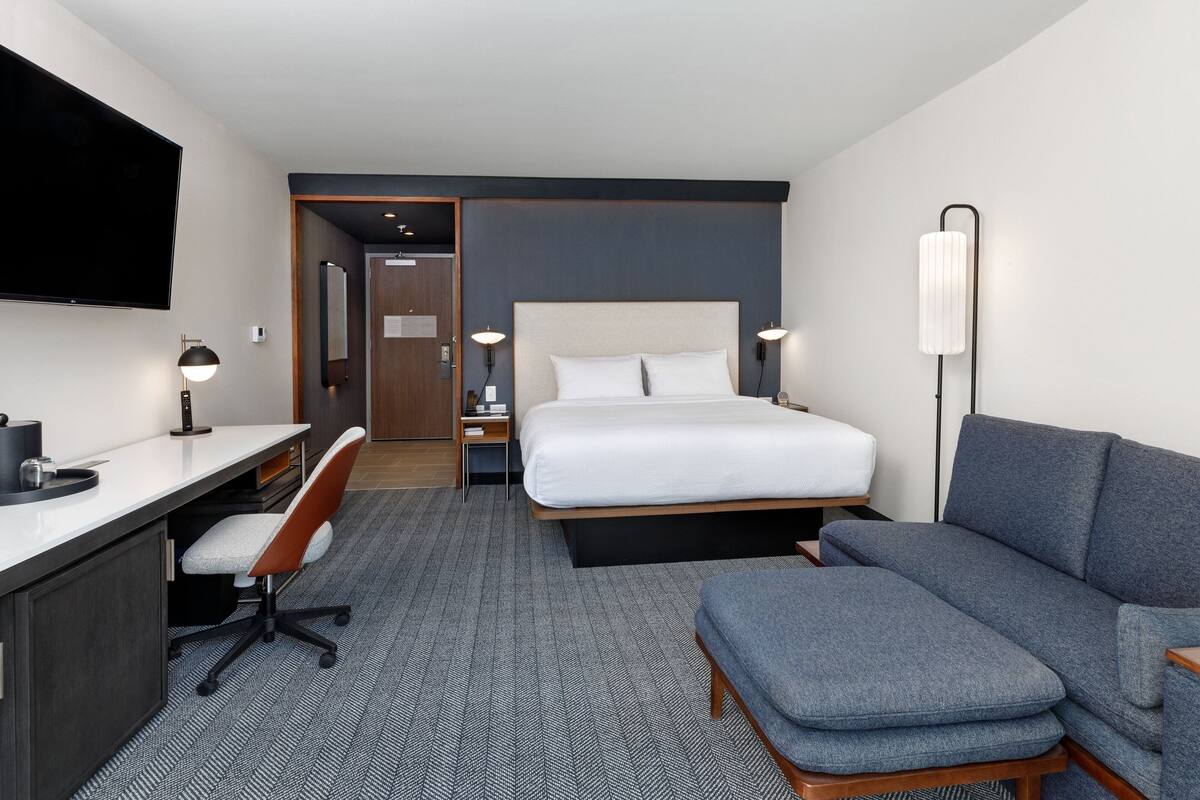 Une chambre d’hôtel équipée d’un lit, d’un bureau, d’une chaise, d’un canapé et d’une télévision.