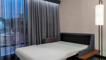 Una habitación de hotel con una cama, una mesita de noche, una lámpara y vistas a un espacio exterior.