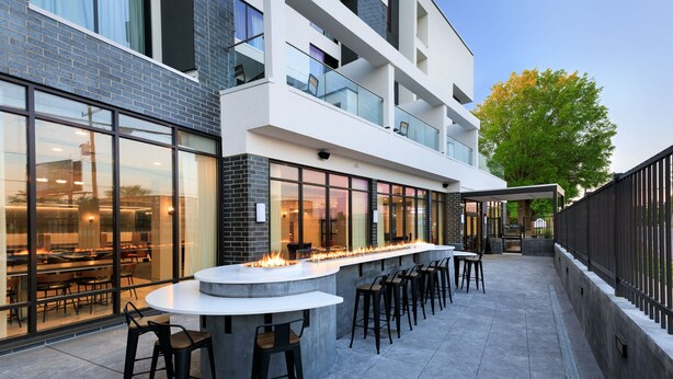 A modern outdoor bar area with a long counter, multiple stools, and a fire feature. - Courtyard by Marriott Richmond Scott’s Addition (Richmond)
