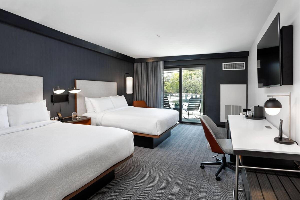 Une chambre d’hôtel avec deux lits, un bureau, une chaise, une télévision et un balcon avec des sièges d’extérieur.