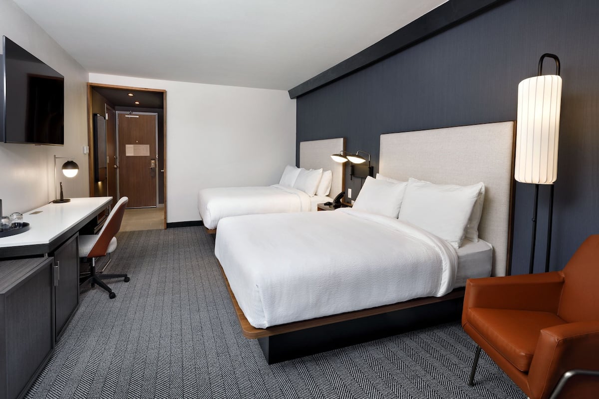 Une chambre d’hôtel avec deux lits, un bureau, une chaise et une télévision.