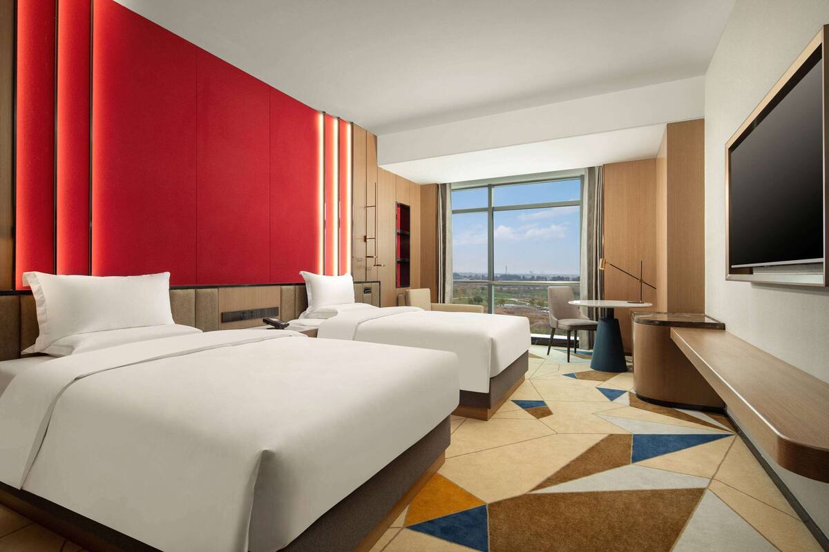 Ein Hotelzimmer mit zwei Betten, einem großen Fenster, einem Fernseher und einem Schreibtisch.