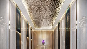 Un pasillo moderno y bien iluminado con suelo de mármol, puertas de vidrio y un techo decorativo.