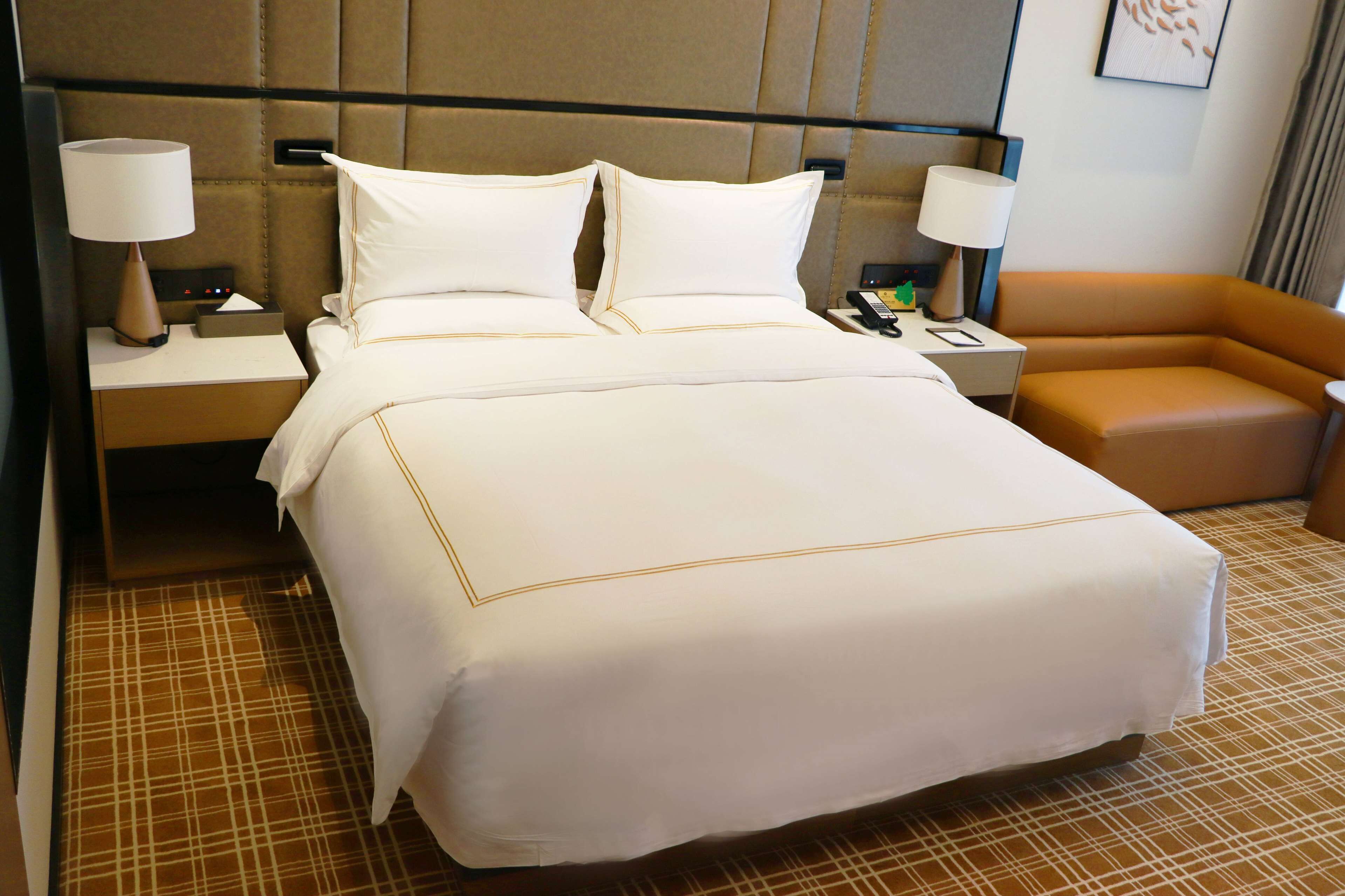 A hotel room with a large bed, two bedside tables with lamps, a small sofa, and a check-in desk.