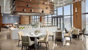 Un comedor moderno con una isla central, diferentes disposiciones de asientos y un techo alto con elementos estructurales a la vista.