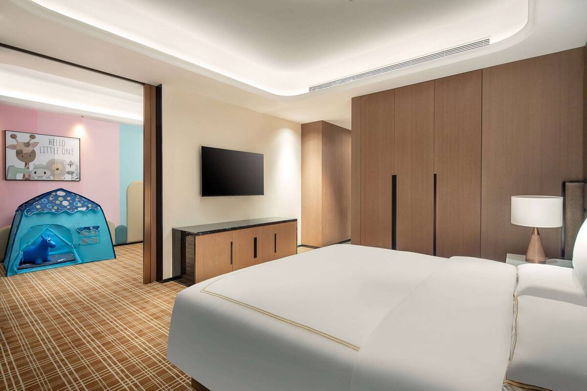 Ein Hotelzimmer mit einem großen Bett, einem flachbildfernseher an der Wand, einem Holzschrank und einer kleinen, zeltartigen Spielecke.