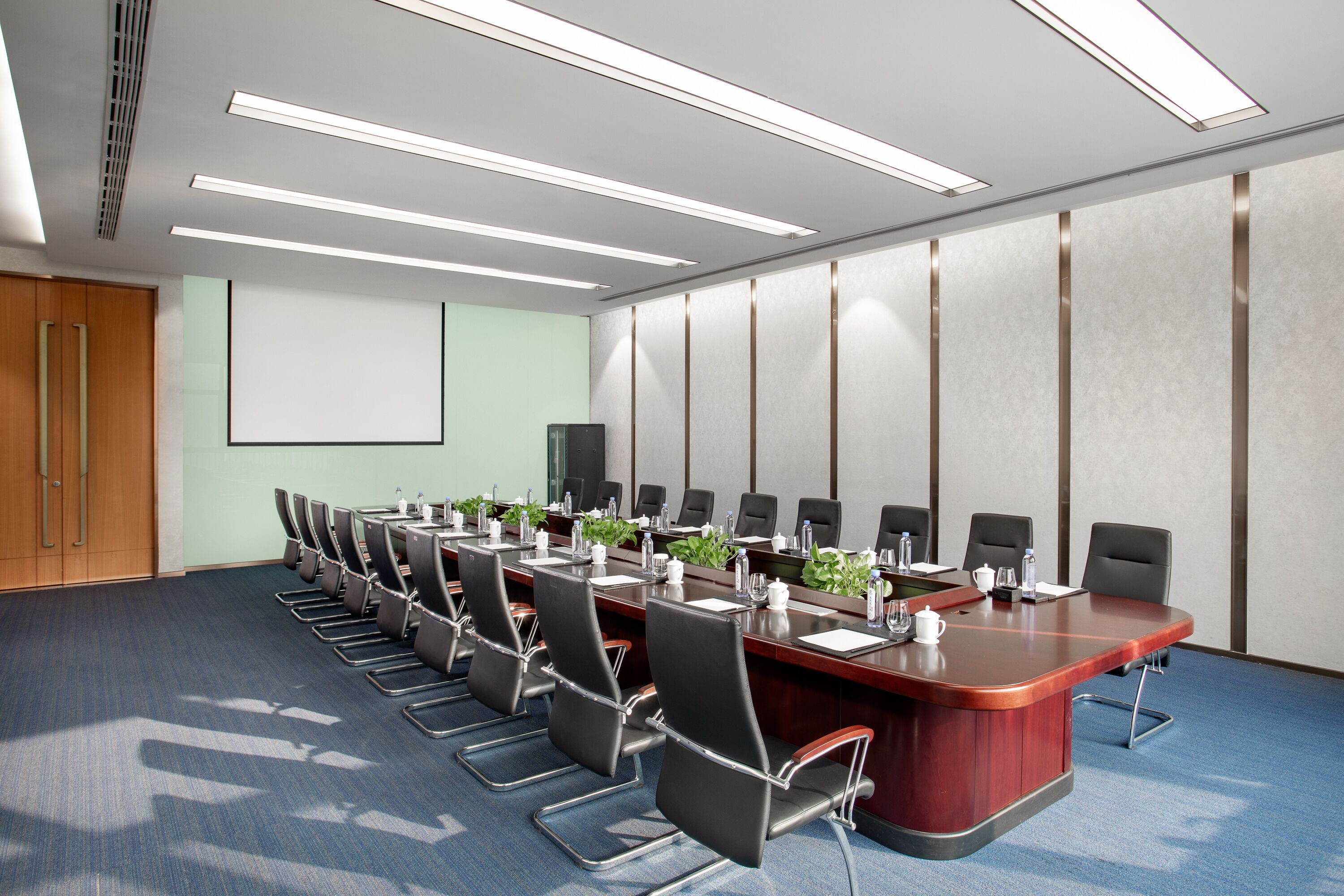A conference room with a long table, chairs, and a projector screen.