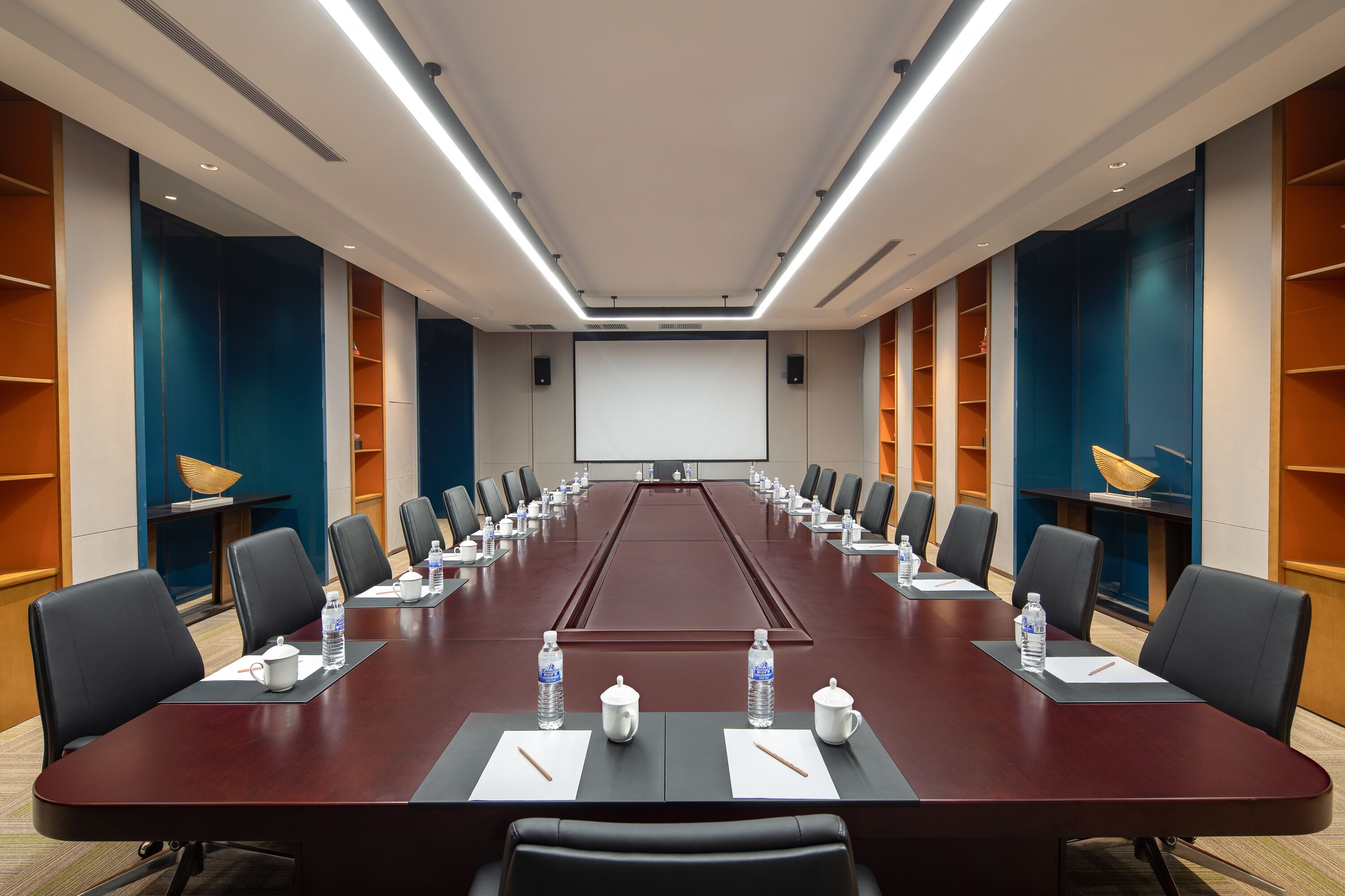 Une salle de conférence avec une longue table, des chaises, des bouteilles d’eau et un écran de projection.