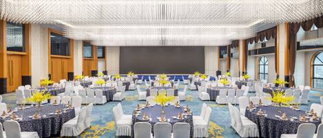 A large conference room with round tables and white chairs, decorated with yellow flowers and blue tablecloths.