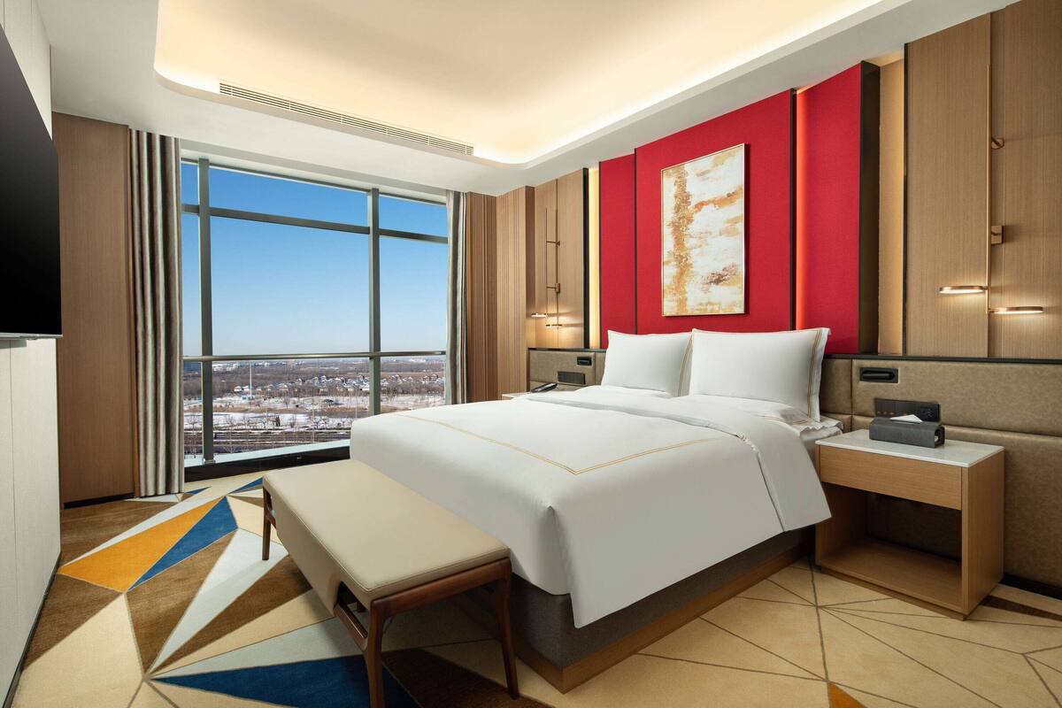 Ein modernes Hotelzimmer mit einem großen Bett, einem Schreibtisch und Blick auf die Stadt.