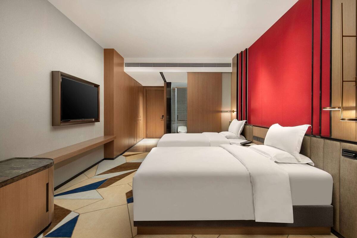 Ein Hotelzimmer mit zwei Betten, einem Fernseher, einem Schreibtisch und einer roten Akzentwand.